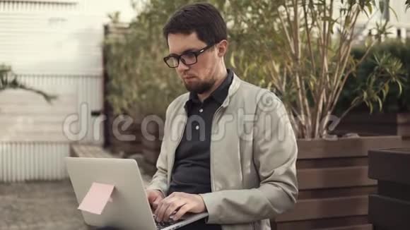 年轻的商人坐在长凳上用笔记本电脑开发一个创业项目视频的预览图
