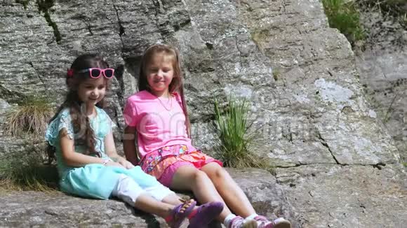 两个漂亮的女孩孩子们坐在岩石的窗台上一只美丽的橙色山蝶旋转着飞过一个孩子视频的预览图