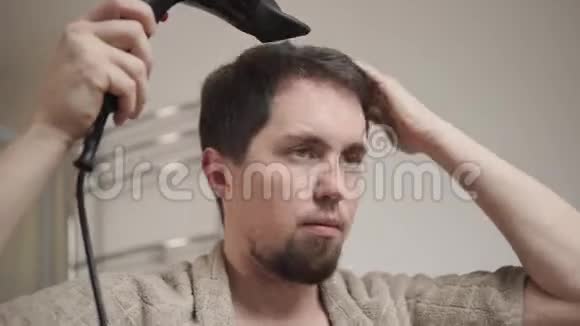 一个年轻人用电吹风机擦干湿发的肖像视频的预览图