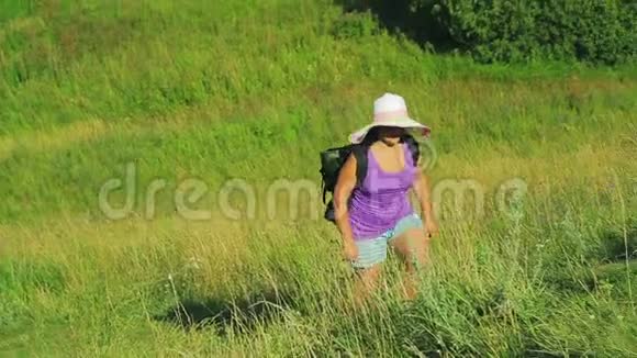 一个戴着草帽背着背包的女人沿着小路爬上了山向侧面射击视频的预览图