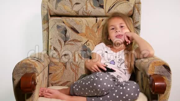 沙发椅上的小女孩用遥控器改变频道模仿她看到的东西视频的预览图