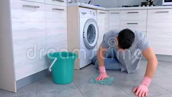 一个穿着橡胶手套的不开心疲惫的男人在厨房里洗地板看着最后的相机视频的预览图