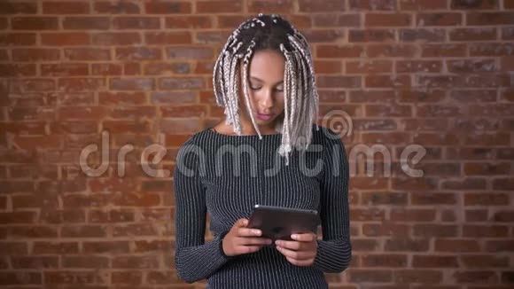 年轻的非洲女孩用平板电脑打字背景中的砖墙视频的预览图