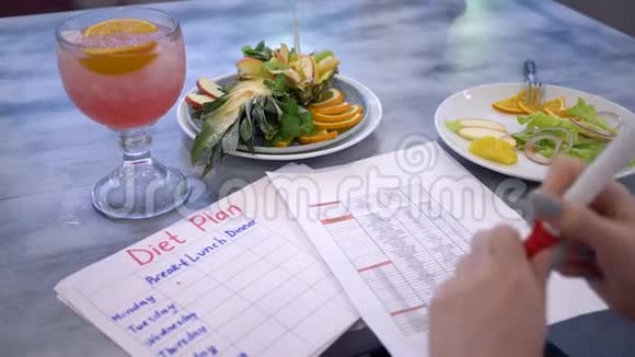 饮食计划用红色标记的女性手在白纸上写下卡路里一词在桌子上的盘子里靠近美丽的食物视频的预览图
