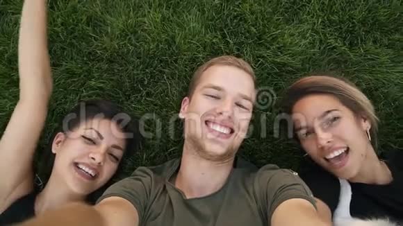 三位迷人的千禧朋友在公园或草坪上躺在绿草上一边自拍高加索人和视频的预览图