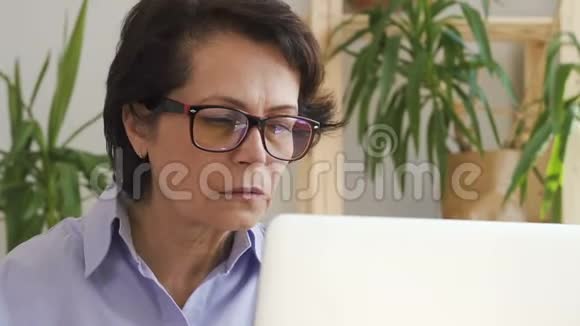 自信的老年妇女在办公室里用笔记本电脑做在线项目视频的预览图