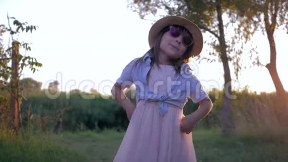 太阳眼镜和草帽的小女孩在村里日落时分在镜头前跳舞的肖像视频的预览图