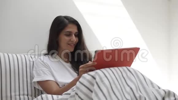一个微笑的女人躺在她房间的床上手里拿着一块药片视频的预览图