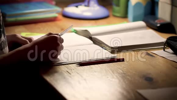 正在学习做家庭作业的男孩少年男孩坐在桌子旁晚上在笔记上写字视频的预览图