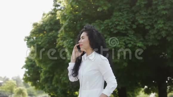 美丽的黑发女郎与朋友通过电话交谈夏季公园视频的预览图
