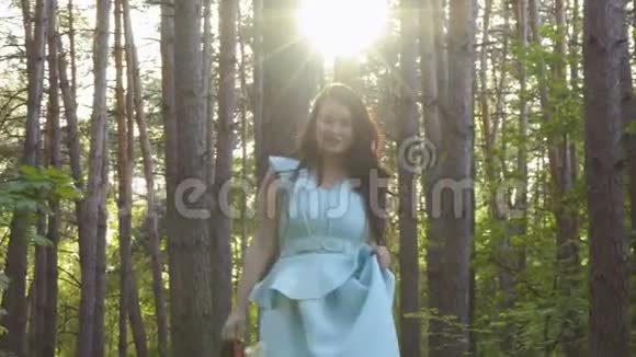 穿着蓝色裙子的黑发美女手里拿着红鞋在森林里散步视频的预览图