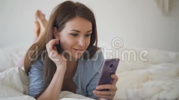 年轻的说谎妇女正在社交媒体上使用智能手机在卧室里交流视频的预览图