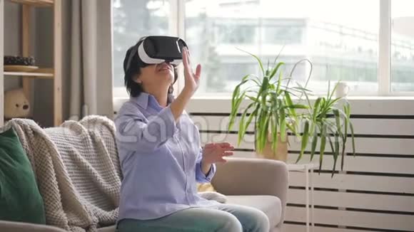 老年妇女正在使用虚拟现实眼镜坐在家里的内部视频的预览图