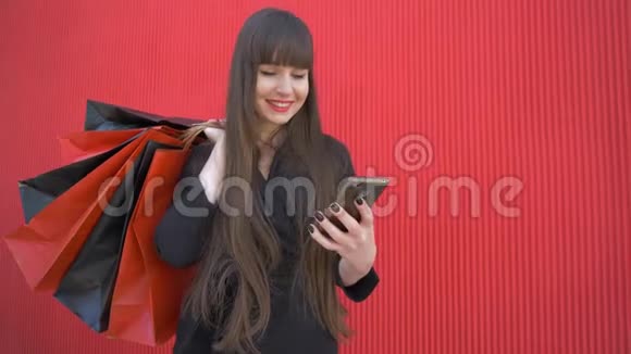 网上购物快乐的女孩使用智能手机带着红色背景的纸袋微笑视频的预览图