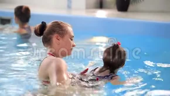 年轻的妈妈在游泳池里慢动作地和她的小女儿玩耍积极生活方式的体育家庭视频的预览图