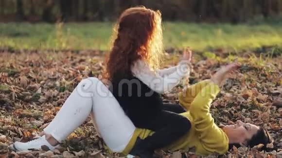 妈妈和女儿手在玩他们在落叶上玩耍秋天公园的幸福家庭视频的预览图