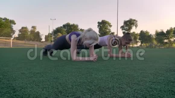 两位年轻漂亮的女士早上在公园的足球场上做木板运动健身模特们锻炼身体视频的预览图