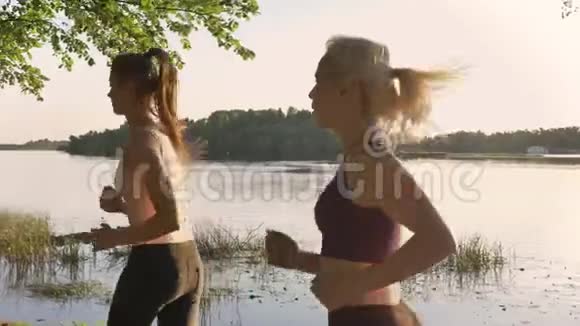 两位年轻漂亮的女跑步者在河边公园慢跑健身模特跑步美丽的自然背景视频的预览图
