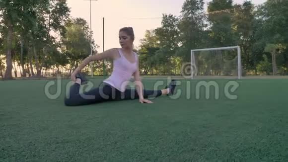 年轻迷人的女人坐在公园的足球场上晨练健身模特伸展视频的预览图