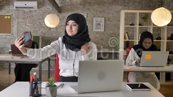 三位年轻的穆斯林妇女戴着头巾坐在现代办公室的笔记本电脑上打字迷人的穆斯林妇女自拍视频的预览图