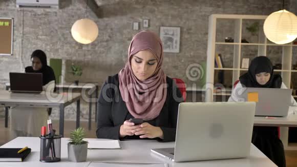 三个年轻的穆斯林妇女戴着头巾坐在现代办公室工作漂亮的女工打电话视频的预览图