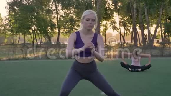 年轻的美女在公园的足球场上伸展其他健身模特在后台锻炼早上锻炼视频的预览图