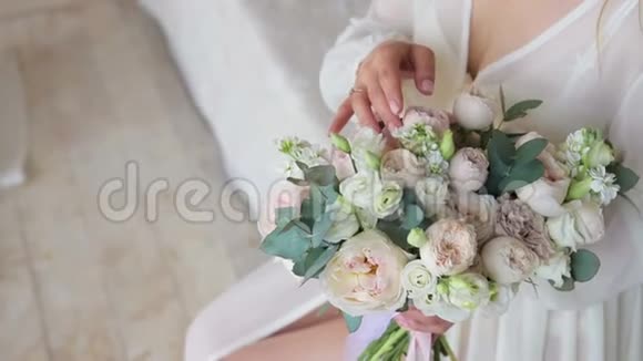 早上好新婚夫妇一位穿着白色睡衣的年轻新娘在床上检查和触摸婚礼花束视频的预览图