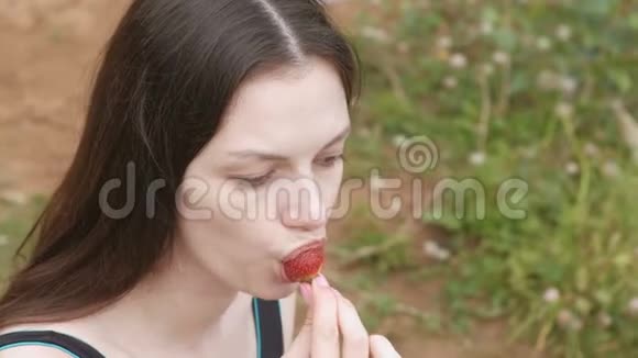 年轻的黑发女人坐在海滩上吃草莓侧视视频的预览图