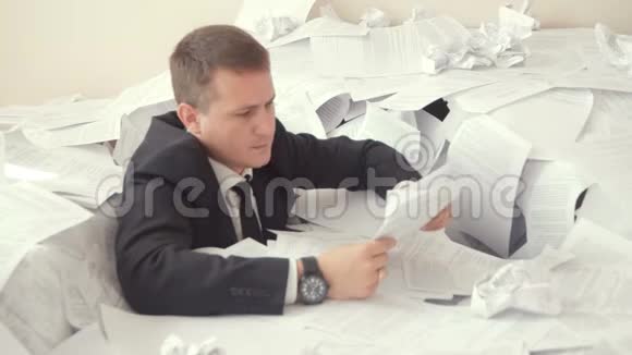 一个疲惫的雇员正坐在办公室里的一堆文件里办公室里的一个年轻人无法应付他的工作视频的预览图