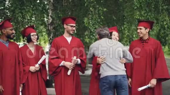 骄傲的父母在大学背景下祝贺学生毕业握手拥抱他们视频的预览图