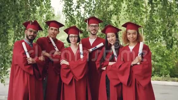 毕业学生抱着毕业证书双臂交叉站在户外的画像视频的预览图