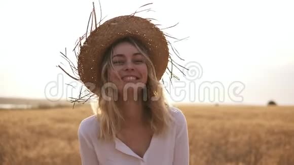 阳光明媚的夏天穿着白衬衫戴着草帽的金发女郎在麦田边走着视频的预览图