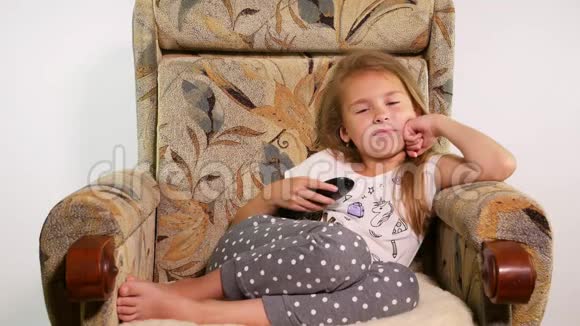 年轻女孩躺在扶手椅上手里拿着遥控器寻找一部有趣的电影视频的预览图