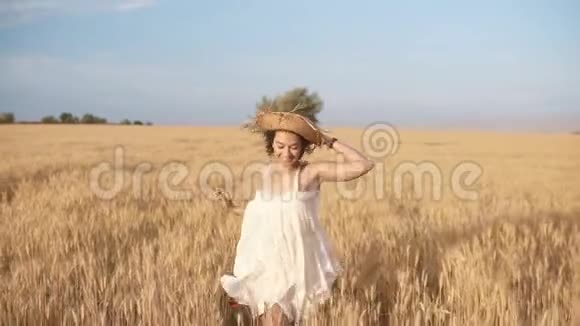 漂亮的年轻女子穿着白色连衣裙在麦田里奔跑微笑快乐的女人奔跑戴着草帽视频的预览图