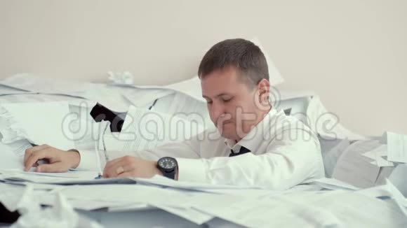 一个疲惫的年轻人坐在一堆文件里在文件上签名由于文件的数量一个办公室工作人员不能视频的预览图