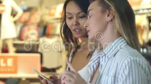 两个年轻漂亮的女购物狂在购物中心上网寻找折扣视频的预览图