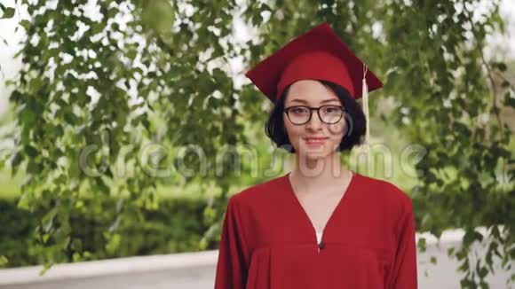 穿着长袍和灰泥板微笑着看着摄像机的年轻女子毕业的肖像视频的预览图