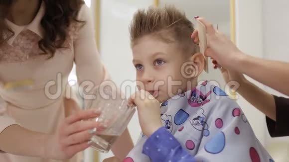 可爱的男孩在理发店为他做发型时喝鸡尾酒视频的预览图