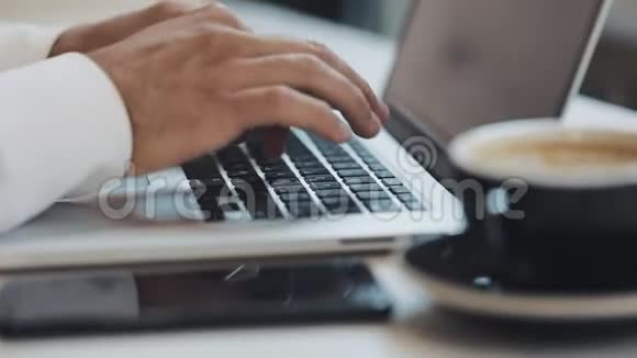 一个男人的手笔记本电脑在咖啡和智能手机的前景在一个咖啡馆休息商人代码业务视频的预览图