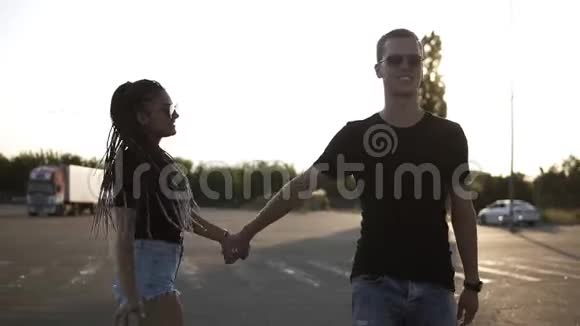 年轻的一对黑发的可怕的女孩戴着太阳镜和她的男朋友走路牵着手太阳照耀着视频的预览图