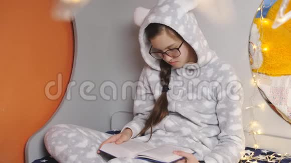 穿着温暖睡衣的女孩在圣诞节休息时坐在床上看书视频的预览图