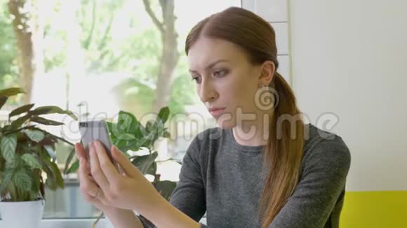 年轻漂亮的女人梳着马尾辫坐在咖啡馆里拿着手机看着电话严肃而关心视频的预览图