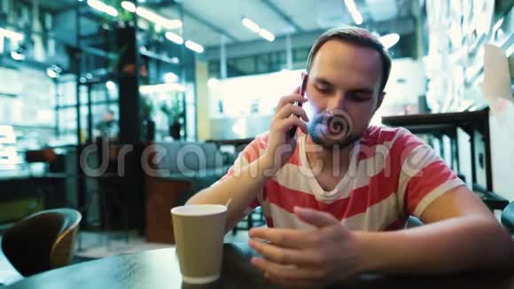 一个留胡子的年轻人坐在城市咖啡馆里打电话视频的预览图