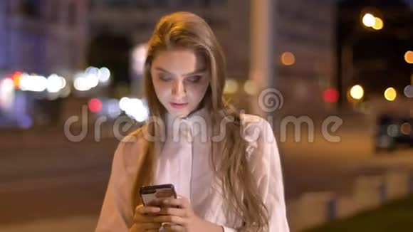 一个年轻漂亮爱做梦的女孩正在夏天晚上在市中心的智能手机上输入信息视频的预览图