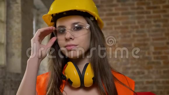 戴着头盔戴着耳机的年轻漂亮的美女戴着相机眨着眼睛微笑着女建筑工人砖头视频的预览图