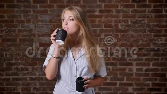 年轻的白种人金发女孩听着耳机里的音乐跳舞喝着咖啡肖像砖墙在里面视频的预览图
