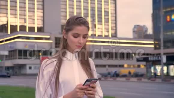 一个年轻漂亮严肃的女孩正在夏季市中心日落时分在智能手机上输入信息视频的预览图