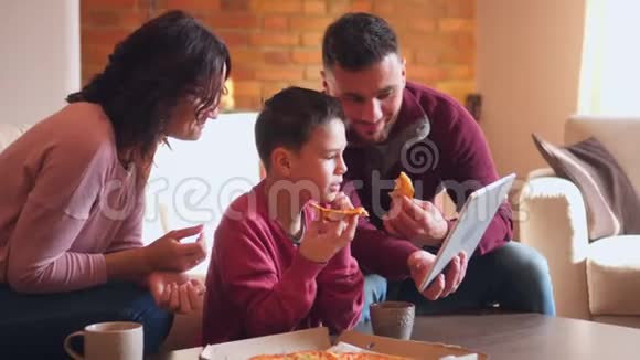 幸福的家庭在客厅吃披萨时使用数码平板电脑视频的预览图