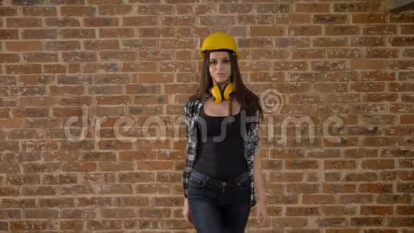 戴着头盔戴着耳机的漂亮漂亮年轻女性走向相机为女建筑工人提供空气钥匙视频的预览图