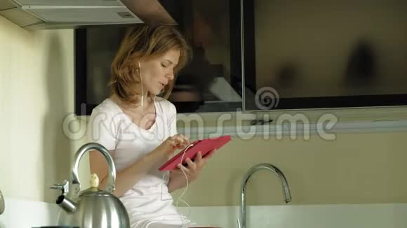 厨房里戴耳机的女人用平板电脑上午视频的预览图